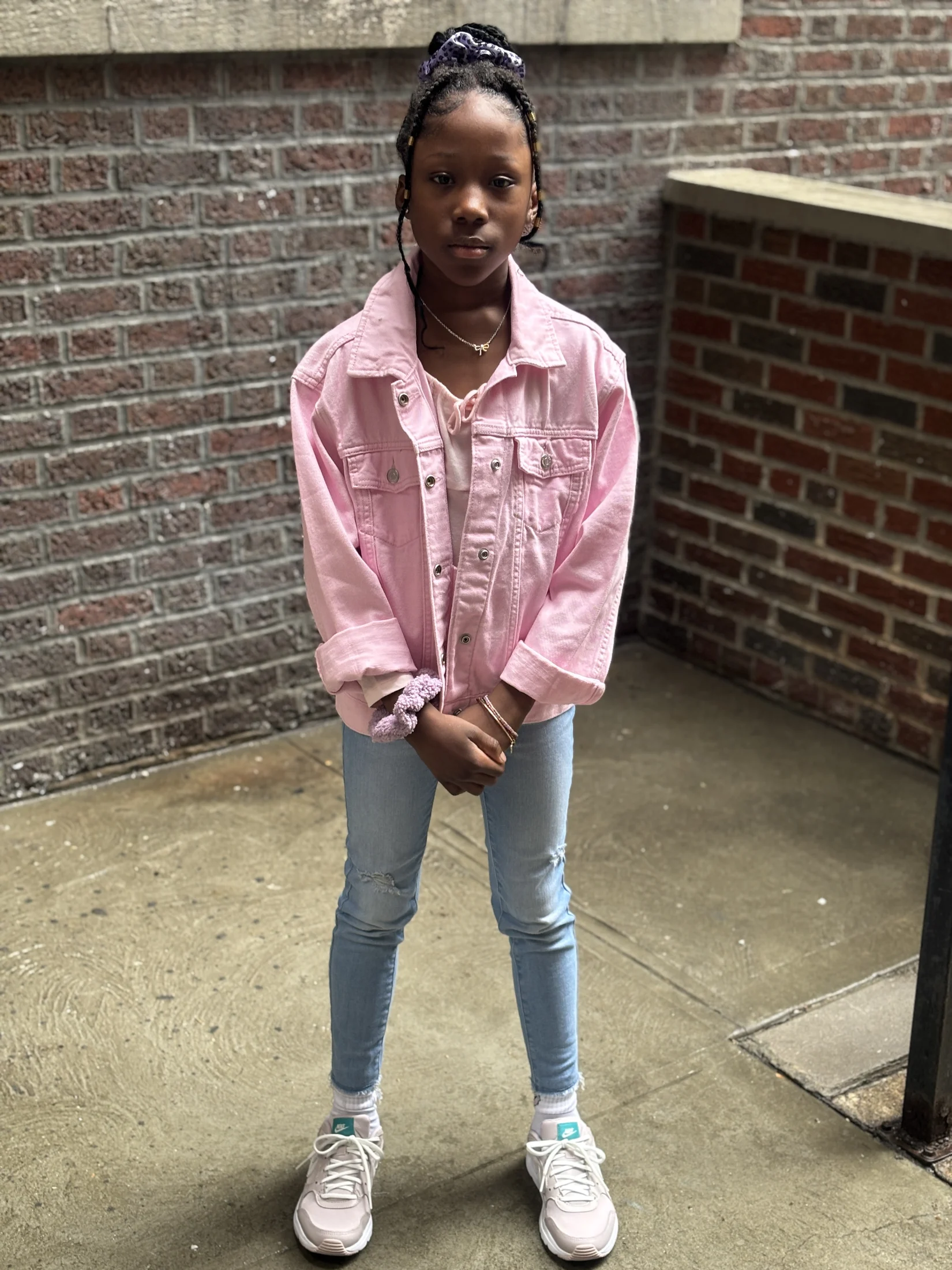 Avi standing outdoors in a pink jacket and jeans